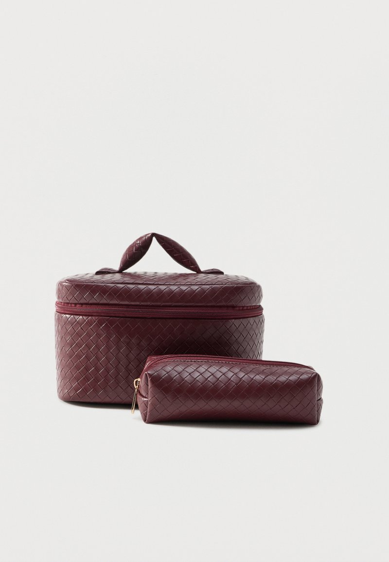 Trousse de maquillage en cuir tressé bordeaux avec poignée et pochette rectangulaire assortie à fermeture éclair sur fond blanc.