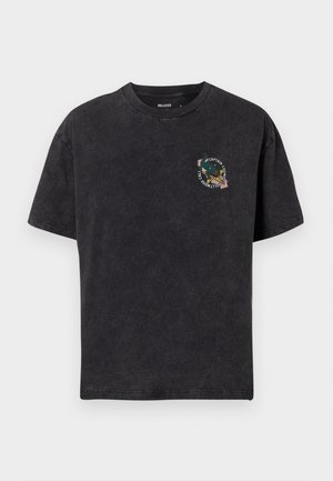 T-shirt nera in cotone a maniche corte con piccolo aquila colorata e scritta "Captain Chomp Hollywood Cal" stampate sul lato sinistro del petto.