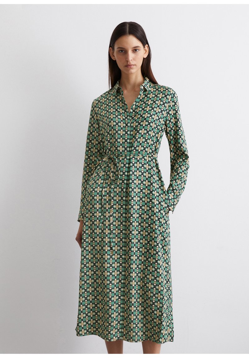 Vestito verde a fantasia con maniche lunghe, colletto e tasche. Presenta disegni geometrici in tonalità gialle, crema e verde scuro.