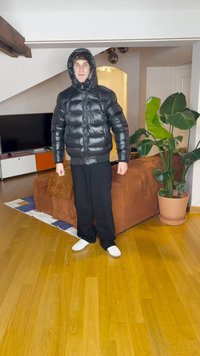 Μαύρο μπουφάν με κουκούλα, μπροστινό φερμουάρ και ριπ κρόσια, σε συνδυασμό με φαρδιά μαύρα παντελόνια και λευκά παπούτσια, σε ένα δωμάτιο με φυτά και έπιπλα.