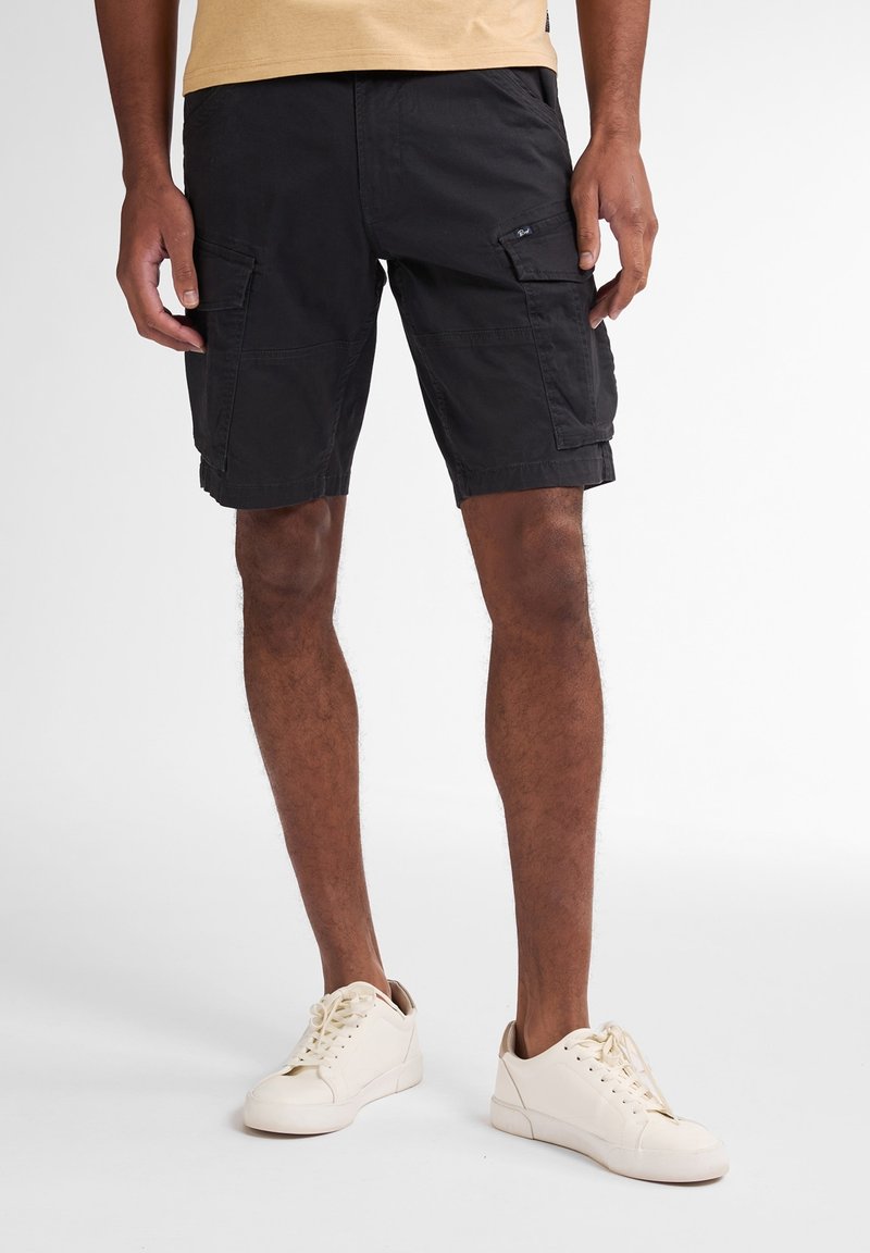 Nederdele i sort cargo-stil lavet af en bomuldsblandingsstof, med sidelommer, afslappet pasform og opfoldede kanter, parret med off-white sneakers.