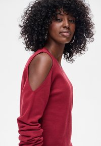 Bordowy sweter z odkrytymi ramionami, o fakturowanym splocie i długich rękawach. Posiada dekolt w serek i dopasowaną sylwetkę.