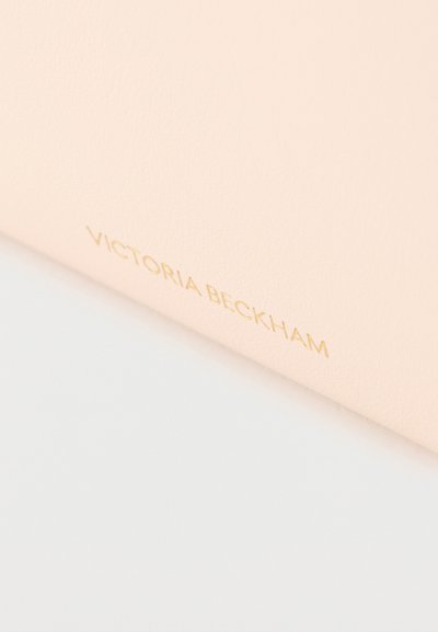 Απαλή ροζ υφή με το κείμενο "VICTORIA BECKHAM" ανάγλυφο σε μικρά, χρυσά κεφαλαία γράμματα κοντά στην άκρη.