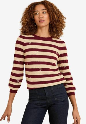 Gestreifter Pullover in Burgunder und Creme mit Schleifenakzenten, gestrickter Textur, Rundhalsausschnitt und 3/4-langen Ärmeln, kombiniert mit dunkelblauen Jeans.