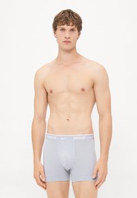 Boxers ajustados Nike grises con una banda de logo blanca, que presentan una textura de tela suave y un diseño entallado, llevados por un modelo masculino.