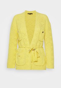 Żółty dziergany kardigan z wzorem diamentowym, dwoma przednimi kieszeniami oraz paskiem do wiązania z detalem w postaci frędzli. Otwarty przód.