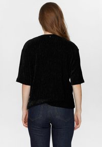 Svart kortärmad topp med en texturerad tyg, med rundad bakhalsringning. Matchas med mörka denimjeans, vilket framhäver casual stil.