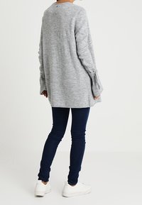 Szary, długi sweter z luźnym krojem i rozcięciami przy mankietach. Połączony z ciemnoniebieskimi dżinsami i białymi trampkami. Miękka dziana tekstura.
