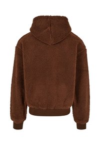 Ruda pūkuota džemperis su tekstūruotu paviršiumi, trumpa iškirpte, kaiščiu ir raukinėtas rankogaliais bei juosmeniu. Rodoma galinė pusė.