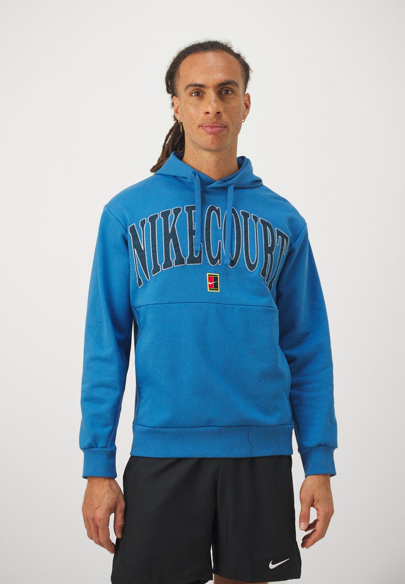 Fleece azul da NikeCourt com bolso frontal, logótipo proeminente em cor contrastante, capuz com cordão e punhos em ribana. Design simples e desportivo.