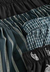 Sammlung von Stoffen mit elastischen Taillen: einfarbig schwarz, dunkelgrün mit Streifen, kariert und mit weißen Mustern. Texturiertes Baumwollmaterial.