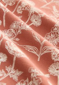 Tissu texturé corail avec des motifs floraux blancs comprenant diverses fleurs et feuilles, présentant un design naturel et délicat.