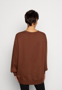 Felpa marrone con vestibilità rilassata, spalle scese e scollatura arrotondata, con polsini e orlo a coste per il massimo comfort.