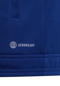 Primer plano de una tela azul con costuras cosidas y un logo de un globo blanco encima del texto "AEROREADY" impreso en la superficie.