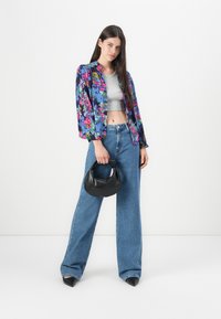 Veste à imprimé floral, crop top gris, jean large taille haute bleu, sac à main noir, escarpins noirs à bout pointu. Présentation propre et moderne.