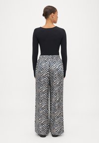 Top preto de mangas longas combinado com calças largas com um padrão de zebra em azul-marinho, creme e castanho. Cintura elástica e design fluido.