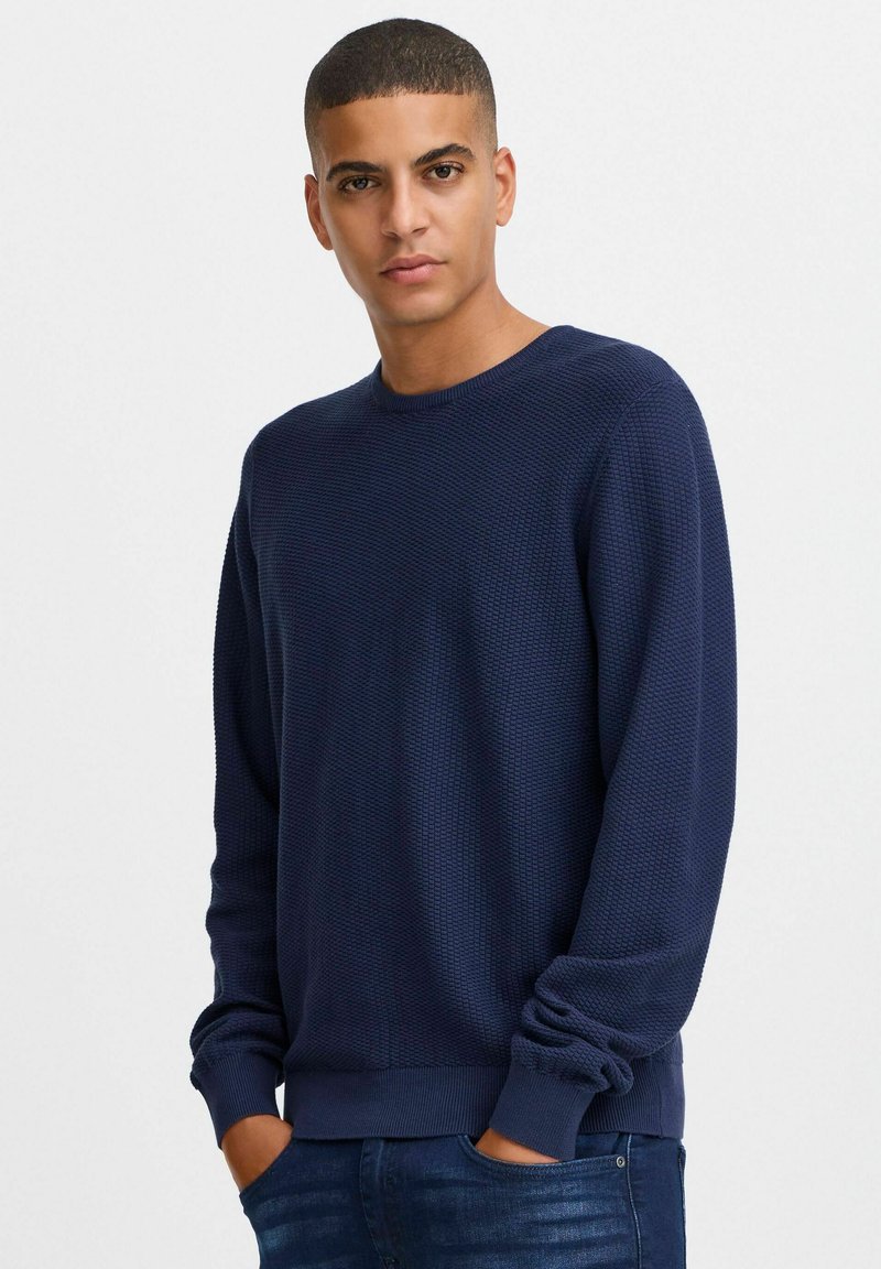 Marineblå, strukturert genser med rund hals og ribbede mansjetter, kombinert med tettsittende jeans. Tøyet har et subtilt mønster.