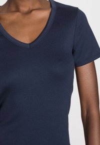 Camiseta de cuello en V azul marino hecha de material de algodón suave; mangas cortas; el diseño ajustado resalta el escote y los hombros.