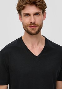 Černé tričko s výstřihem do V, vyrobené z bavlny, s krátkými rukávy, které má hladkou texturu a jednoduchý design, těsně obepínající krk.