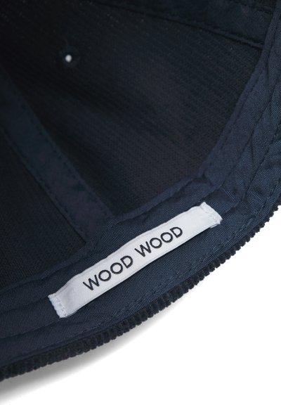 Jūras spēku auduma cepure ar teksturētu iekšpusi, ar šūtu etiķeti, uz kuras melnā tekstā uz balta fona rakstīts "WOOD WOOD".