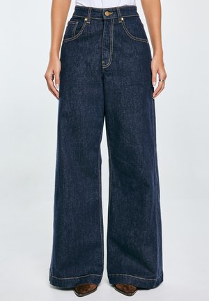 Granatowe spodnie typu wide-leg wykonane z denimu, z złotymi przeszyciami, przednimi kieszeniami oraz wysokim stanem z zapięciem na guzik.