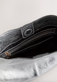 Ezüst bőr kézi táska cipzáros záródással és belső zsebekkel. Simább külső textúra, megerősített szélek és fekete szövet bélés.