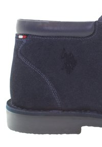 Botín de ante azul marino con un cuello de cuero suave, costuras en contraste y un sutil logo grabado en el lateral. Suela de goma duradera.