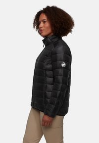 Svart puffjacka med quiltad design, hög krage och dragkedja framtill. Har sidofickor och en logotyp på vänster ärm.