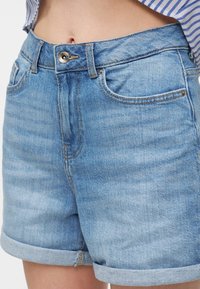 Light blue denim shorts with rolled cuffs, front button, and zipper fly worn by a person in a striped top.