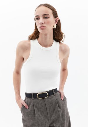 Top de tirantes blanco con cuello redondo, con ribete beige. Combinado con pantalones de tiro alto gris texturizados y un cinturón negro con hebilla dorada.