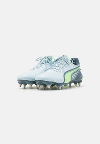 Botas de fútbol de color azul claro con una parte superior texturizada, acentos verdes y una suela resistente con detalles en blanco y gris.