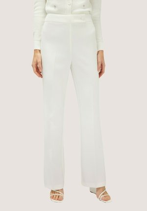 Pantaloni bianchi su misura con gamba dritta, texture liscia, vita alta e discreta fantasia a righe sottili, abbinati a semplici sandali bianchi.