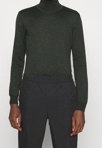 Donkergroene coltrui in een geribde textuur, met een aansluitend ontwerp en lange mouwen, gecombineerd met zwarte broek met elastische taille.