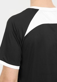 Svart atletisk T-shirt med vit kant längs axeln, tillverkad av lättviktsmaterial med en mjuk textur.