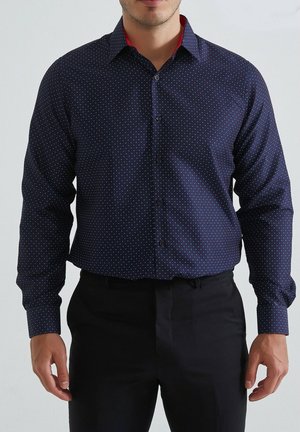 Chemise boutonnée marine avec petits points blancs et rouges, col intérieur rouge contrastant, manches longues et coupe standard.