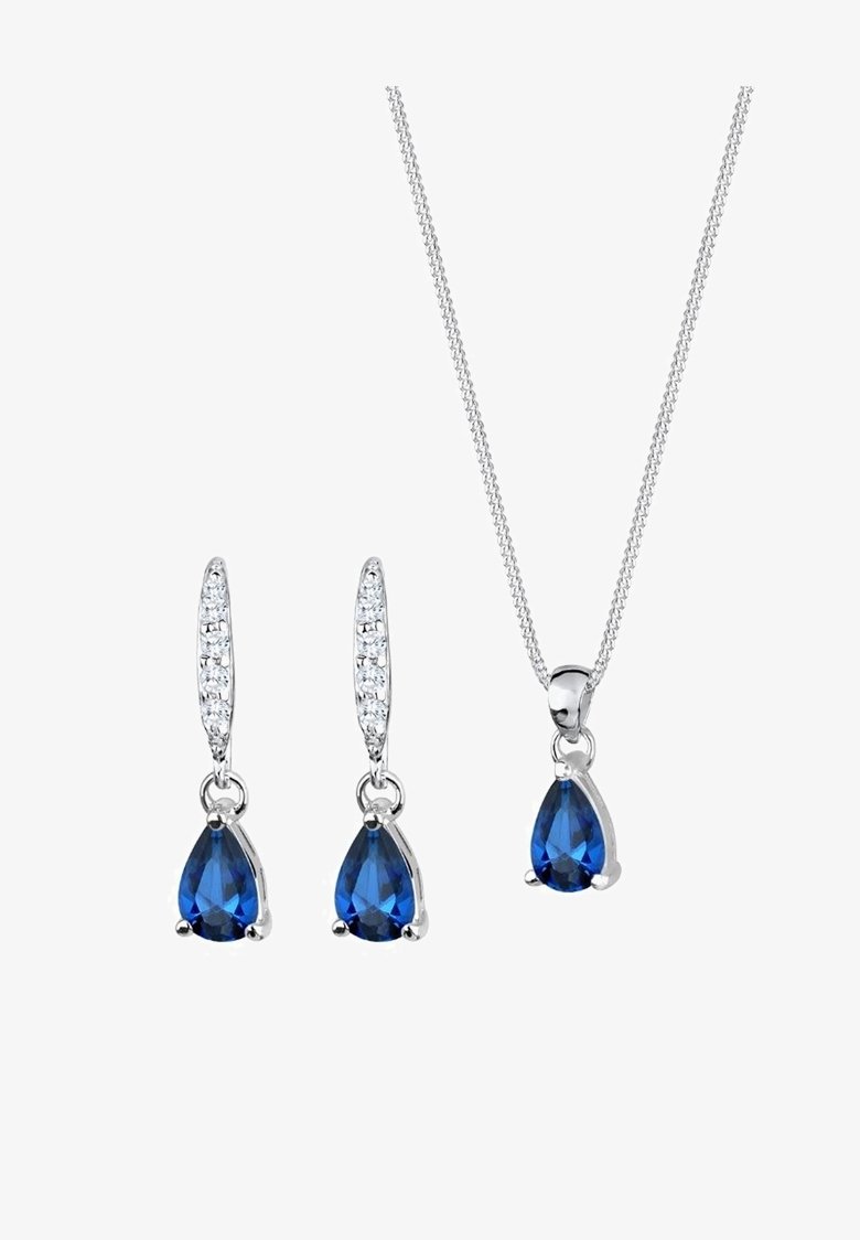 Collier en argent et boucles d’oreilles assorties avec des pierres précieuses bleues en forme de goutte et de petits cristaux clairs sur fond blanc.