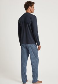 Haut à manches longues bleu marine associé à un pantalon de pyjama bleu motif géométrique, fabriqué en tissu doux et avec une coupe décontractée.