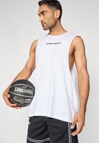 Λευκό αμάνικο αθλητικό τοπ με λογότυπο «UNDER ARMOUR», συνδυασμένο με μαύρο σορτς από δίχτυ με λευκές λεπτομέρειες, κρατώντας μια μαύρη μπάλα του μπάσκετ Spalding.