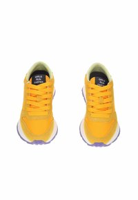 Geel sneaker van mesh en suède materialen, ronde neus, platte paarse zool en oranje accenten. Bevat "GIRLS RUN FASTER" op de tong.