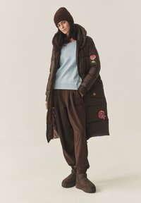 Barna pehelykabát virágos hímzéssel, világoskék pulóver mackós mintával, barna nadrág és barna csizma. Mindenhol lágy tapintású anyagok.