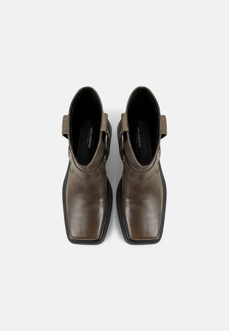 Ein Paar braune Leder-Stiefeletten mit quadratischer Zehenform und schwarzen Sohlen sowie seitlichen Riemen, von oben auf einem weißen Hintergrund betrachtet.