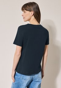 Sort kortærmet t-shirt med rund halsudskæring, glat tekstur og en let afslappet pasform. Båret med lyseblå denim jeans.