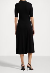 Svart, knälång klänning med korta ärmar, en åtsittande livdel och utsvängd kjol. Har en krage och en slät tygstruktur.