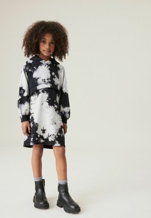 Robe tie-dye noire et blanche avec capuche, manches longues et coupe loose, portée avec des bottines noires et des chaussettes grises.