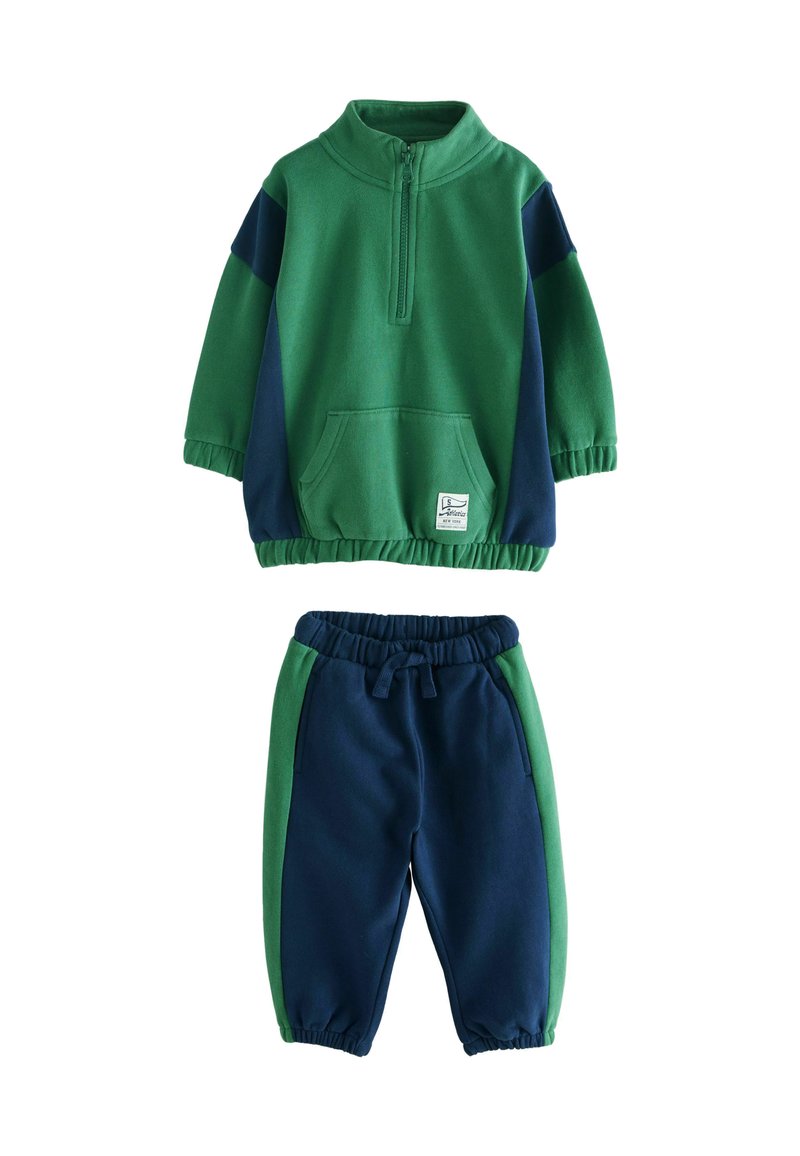 Grønne og marineblå fleece-træningssæt til børn med en pullover med halvlynlås og bukser med elastisk talje, der har en kængurulomme og kontrasterende sidepaneler.
