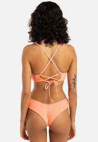 Ribbed two-piece bikini in light pink with crisscross strap detail and a tied back. The bottom has a moderate coverage design.
