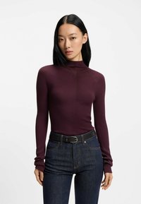 Burgundy-ribbad långärmad tröja med hög krage, bärs med mörka denimjeans och ett svart bälte. Tyget har en subtil textur.