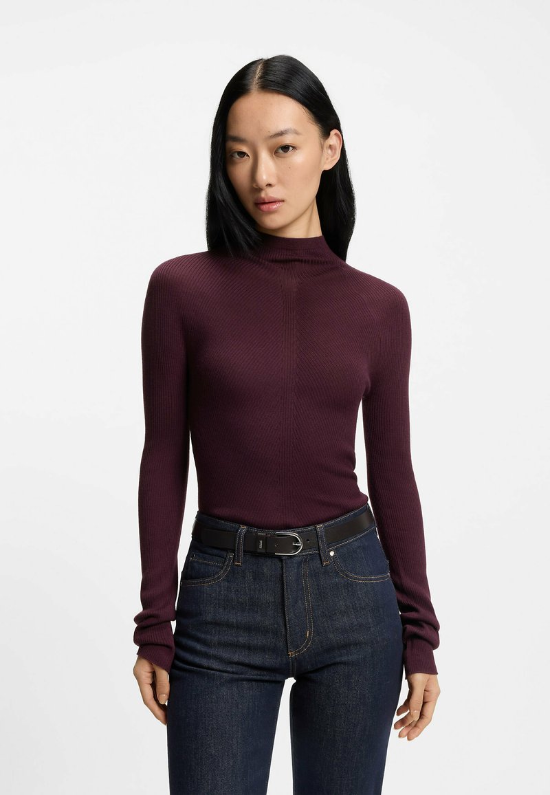 Burgundy-ribbad långärmad tröja med hög krage, bärs med mörka denimjeans och ett svart bälte. Tyget har en subtil textur.