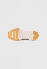 Sole of a sneaker with light brown rubber heel and toe areas and white middle section with triangular tread patterns.