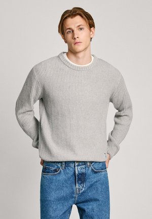 Szary sweter z prążkowanym wzorem, z okrągłym dekoltem i długimi rękawami, wykonany z dzianiny. Nosi się go na białej koszuli, w zestawieniu z niebieskimi dżinsami.